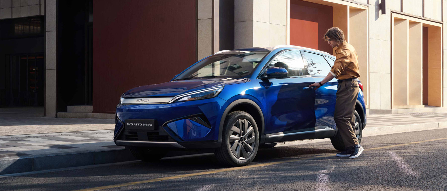 En person åbner førerdøren på en blå BYD Atto 3 el-SUV, der står parkeret på en gade i byen om dagen.
